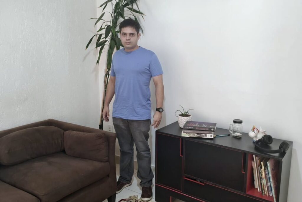 A sala de atendimento: sofá, tapete e a estante de livros, com Felipe Rippel em pé ao lado